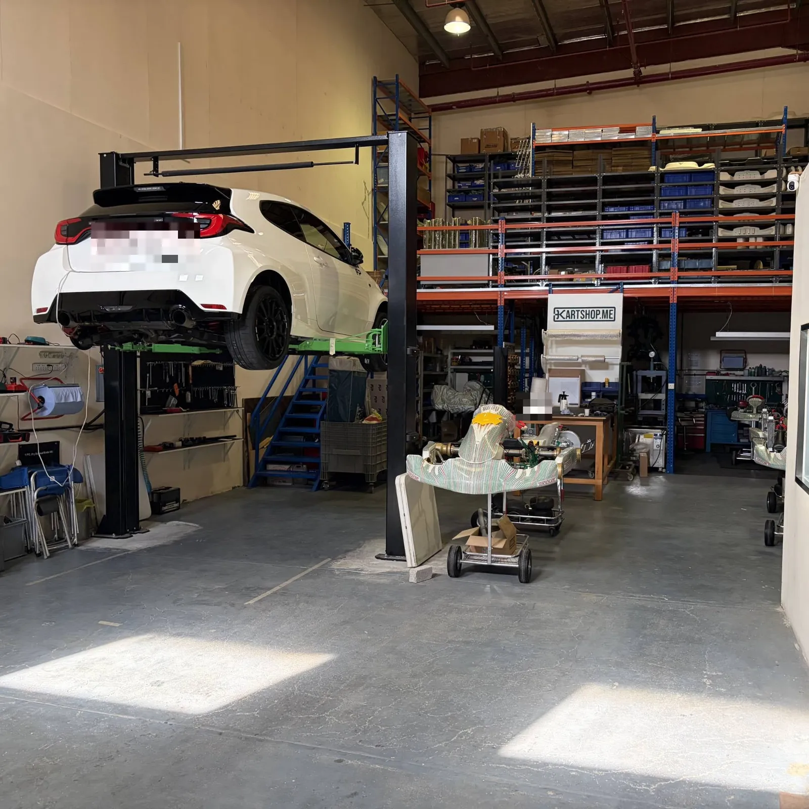 Scuderia's Dubai warehouse with a car on the lift, parts shelving and karts